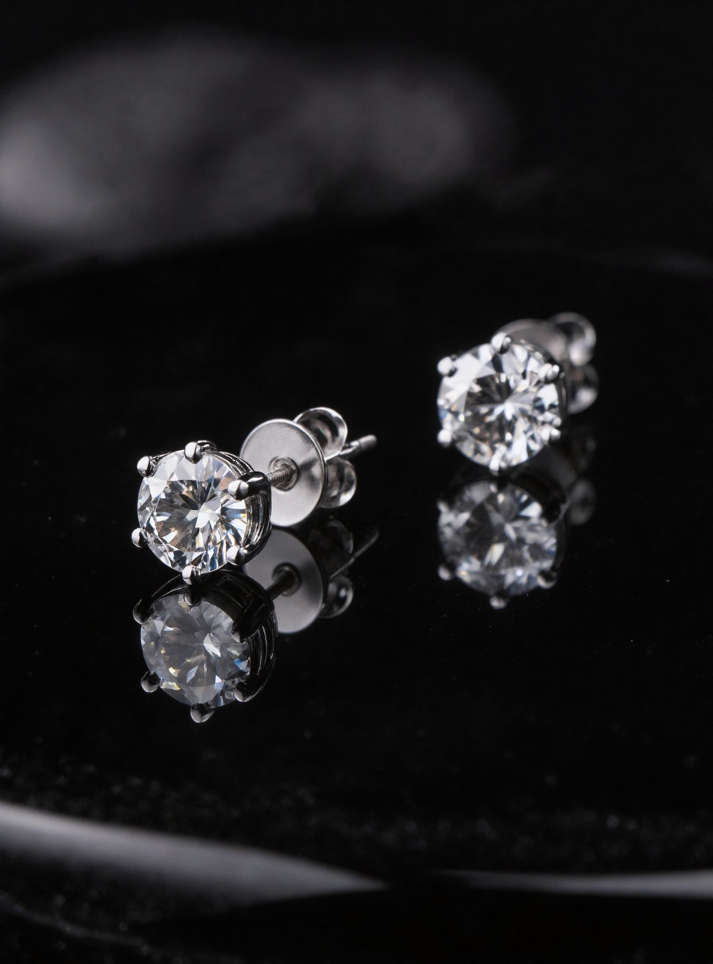 Pair of moissanite stud earrings on a reflective black surface
