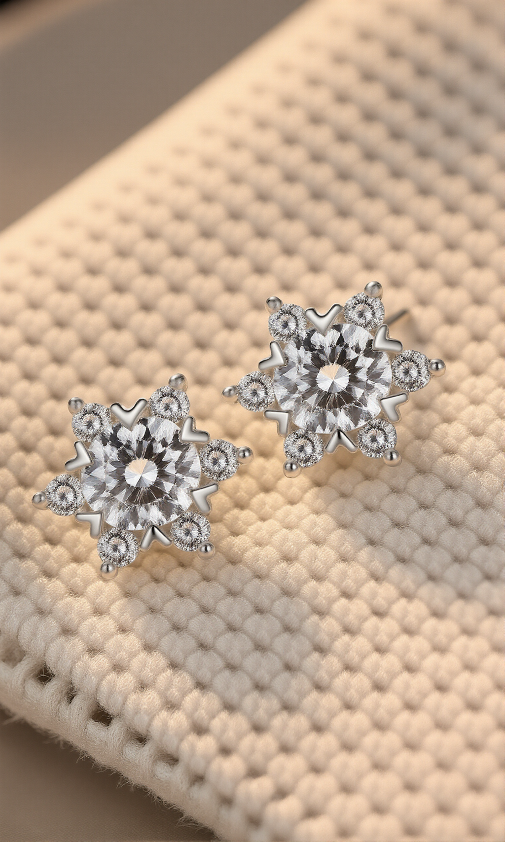 Pair of snowflake-shaped silver earrings on a textured beige surface