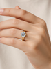 Gold ring with a moissanite on a hand against a neutral background