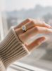 Hand wearing a gold ring with a moissanite, blurred background